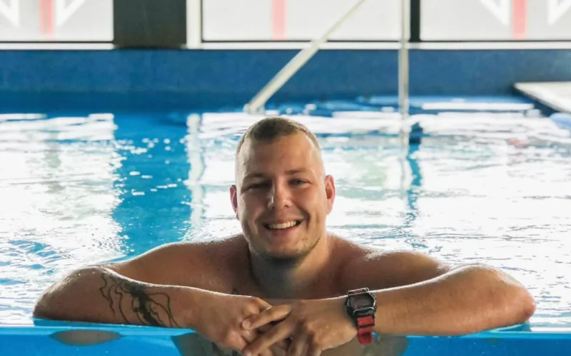Wojtek Kacik, instruktor pływania AquaJoy, oparty o brzeg basenu